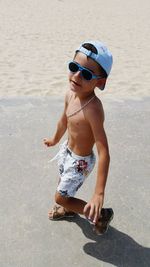 Portrait of shirtless boy wearing sunglasses while walking on footpath by beach