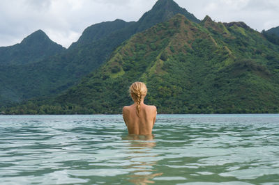 Rear view of shirtless man in lake against mountains