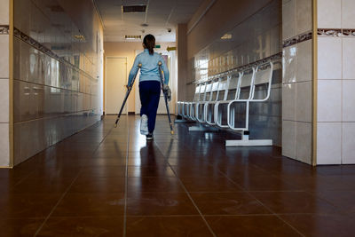 Child walks along hospital corridor on crutches to see doctor. girl has one leg broken in cast.