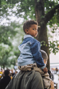 Boy looking away while sitting on father's shoulder at flea market