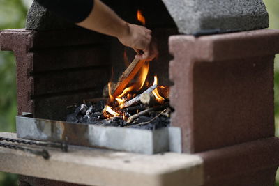 Midsection of man putting firewood in fireplace outdoors