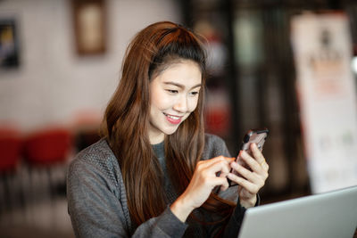 Smiling woman using mobile phone while sitting in cafe