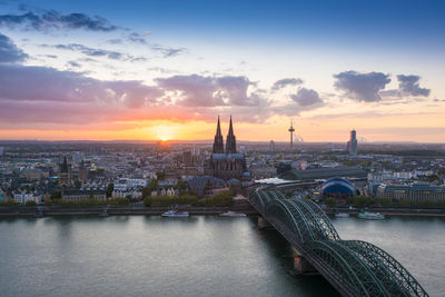 Bridge over river in city against sky during sunset