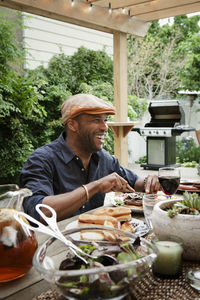 Happy man having food while sitting at table in yard