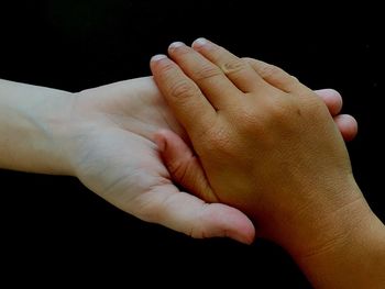 Close-up of hands holding baby hand against black background