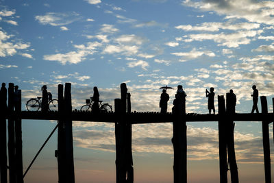 Silhouette people on railing against sky during sunset