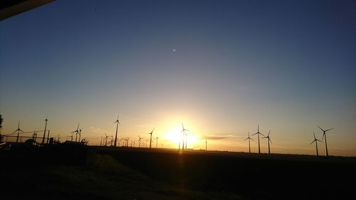 Silhouette wind turbines on field against sky during sunset