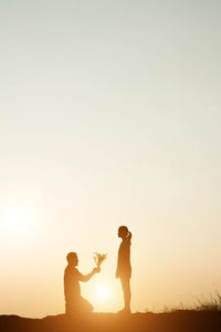 Silhouette man proposing woman against sky during sunset