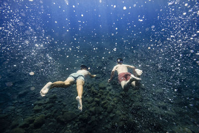 Friends swimming together amidst bubbles undersea
