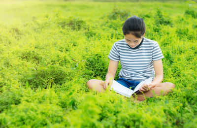 Girl reading book while sitting on grassy field