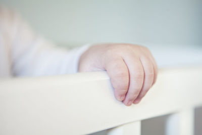 Cropped hand of baby holding crib at home