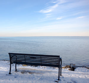 Empty bench by sea against sky