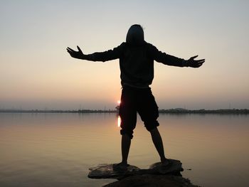 Full length of silhouette man standing by lake against sky during sunset