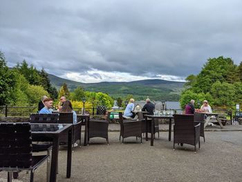 People sitting on bench by trees against sky