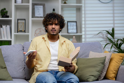 Portrait of young man using mobile phone while sitting on sofa at home