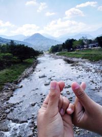 Cropped image of hand with water against sky