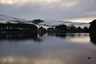 Scenic winter view over lake to trees and snowy hills against sky 