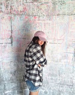 Woman wearing hat standing against wall