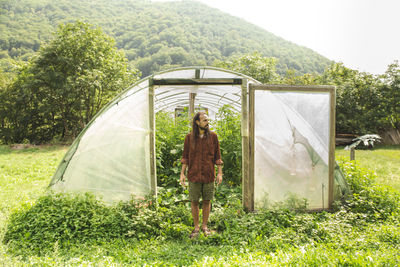 Young farmer standing in front of greenhouse