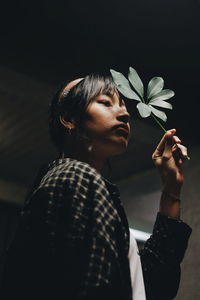 Portrait of young woman holding flower in standing against black background