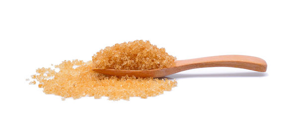 Close-up of brown sugar with wooden spoon against white background