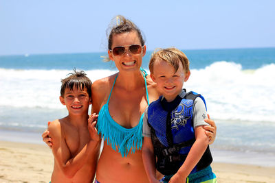 Portrait of cheerful mother with sons at beach on sunny day