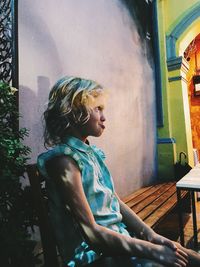 Woman looking away while sitting on building