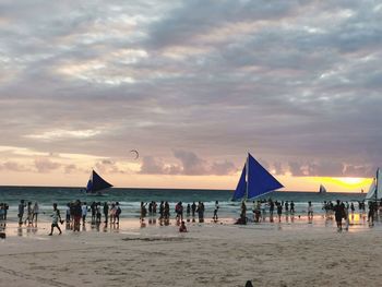 People at beach against sky during sunset