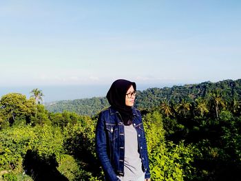 Woman looking away while standing against sky