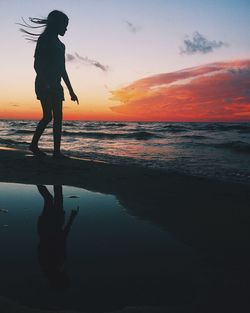 Silhouette man standing on beach against sky during sunset