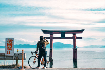 Man riding bicycle by sea against sky