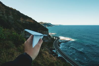 Cropped image of hand holding paper airplane against sea