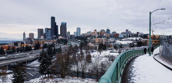 Snow covered road by buildings against sky during winter