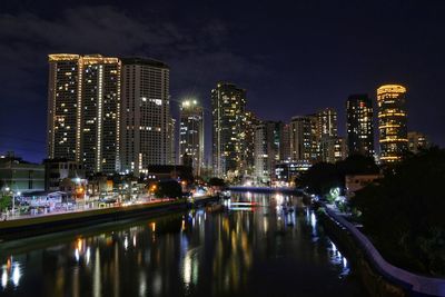 Illuminated buildings by river against sky at night