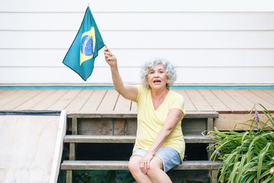 Portrait of senior woman holding brazilian flag sitting on steps