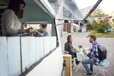 Owners working at food truck while customers sitting in background