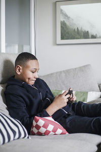 Teenage boy using mobile phone on sofa in living room