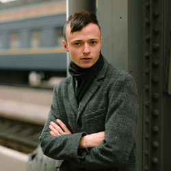 Portrait of young man with arms crossed standing at railroad station