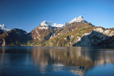 Scenic view of lake and mountains against clear blue sky