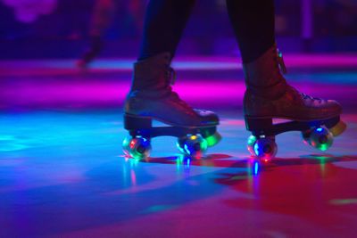 Low section of person roller skating on floor in illuminated rink