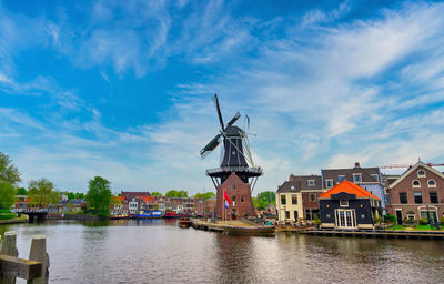 Traditional windmill by canal and buildings against sky