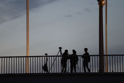 Low angle view of people standing on railing against sky