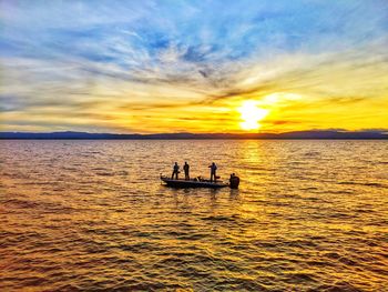 Silhouette people in sea against sky during sunset