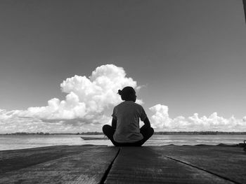 Rear view of man sitting on beach against sky