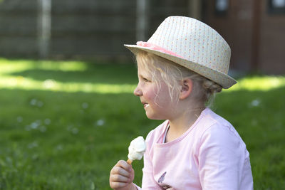 Cute girl eating ice cream while siting on field at park