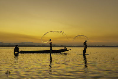 Silhouette people on sea against sky during sunset