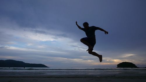 Man jumping on beach against sky during sunset