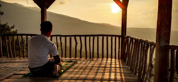 Rear view of man sitting on railing against mountain