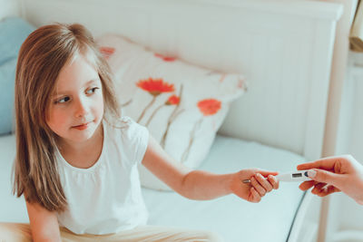 Cropped hand of mother giving thermometer to daughter sitting on bed