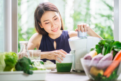 Young woman preparing juice on table at home